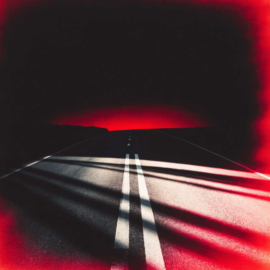 Empty road at dawn, crimson light bleeding out of darkness